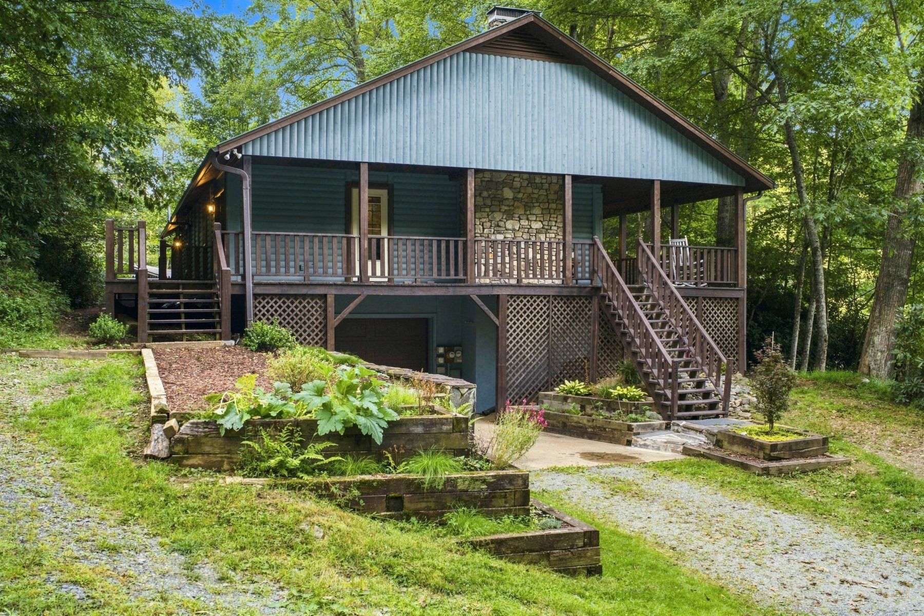 The log cabin's front porch, stone chimney and raised garden beds among tall trees